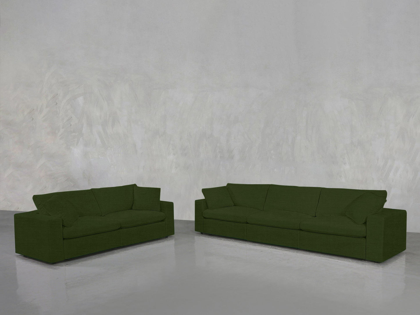 The 3-2 Sofa Set, featuring both a smaller and larger green sofa, is arranged on a shiny grey floor against a textured light grey wall in a minimalist, empty room.
