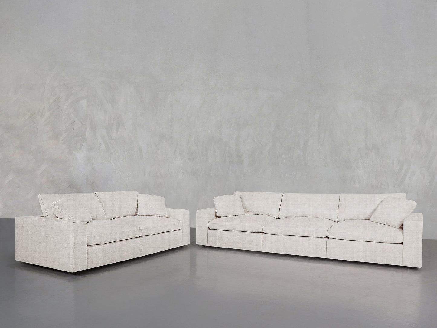 The 3-2 Sofa Set, featuring modern cream upholstery with square arms and plush cushions, is arranged on a smooth gray floor against a light gray textured wall.