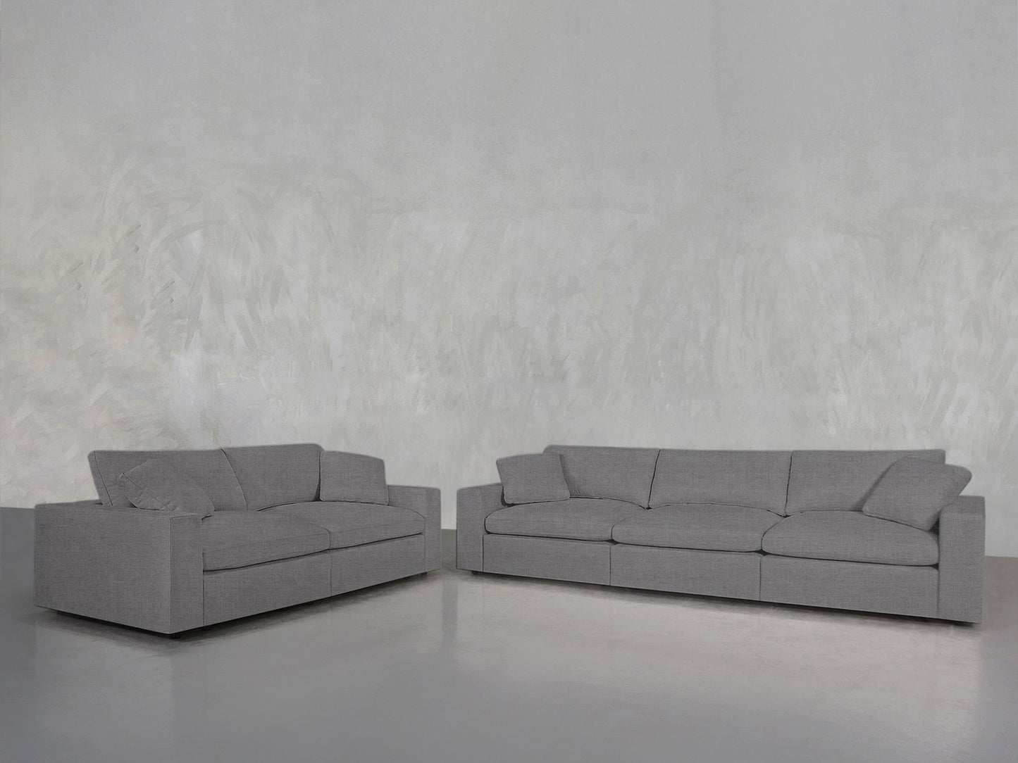The 3-2 Sofa Set features two modern gray sofas with clean lines, arranged in an L-shape against a light gray textured wall and reflective floor. Both sofas have matching cushions and a minimalist design.
