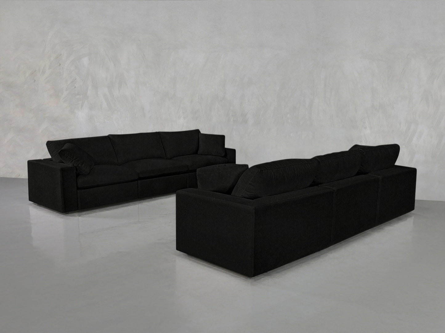 A pair of 3-3 Sofa Set pieces, featuring thick cushions and a modern black design, are arranged in a minimalist room with light gray walls and a glossy floor.