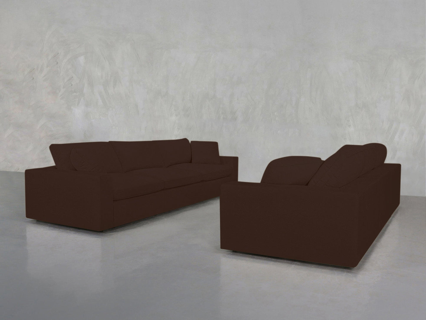 A pair of 3-3 Sofa Sets in dark brown are arranged at an angle in a minimalist room with plain light gray walls and a polished concrete floor.