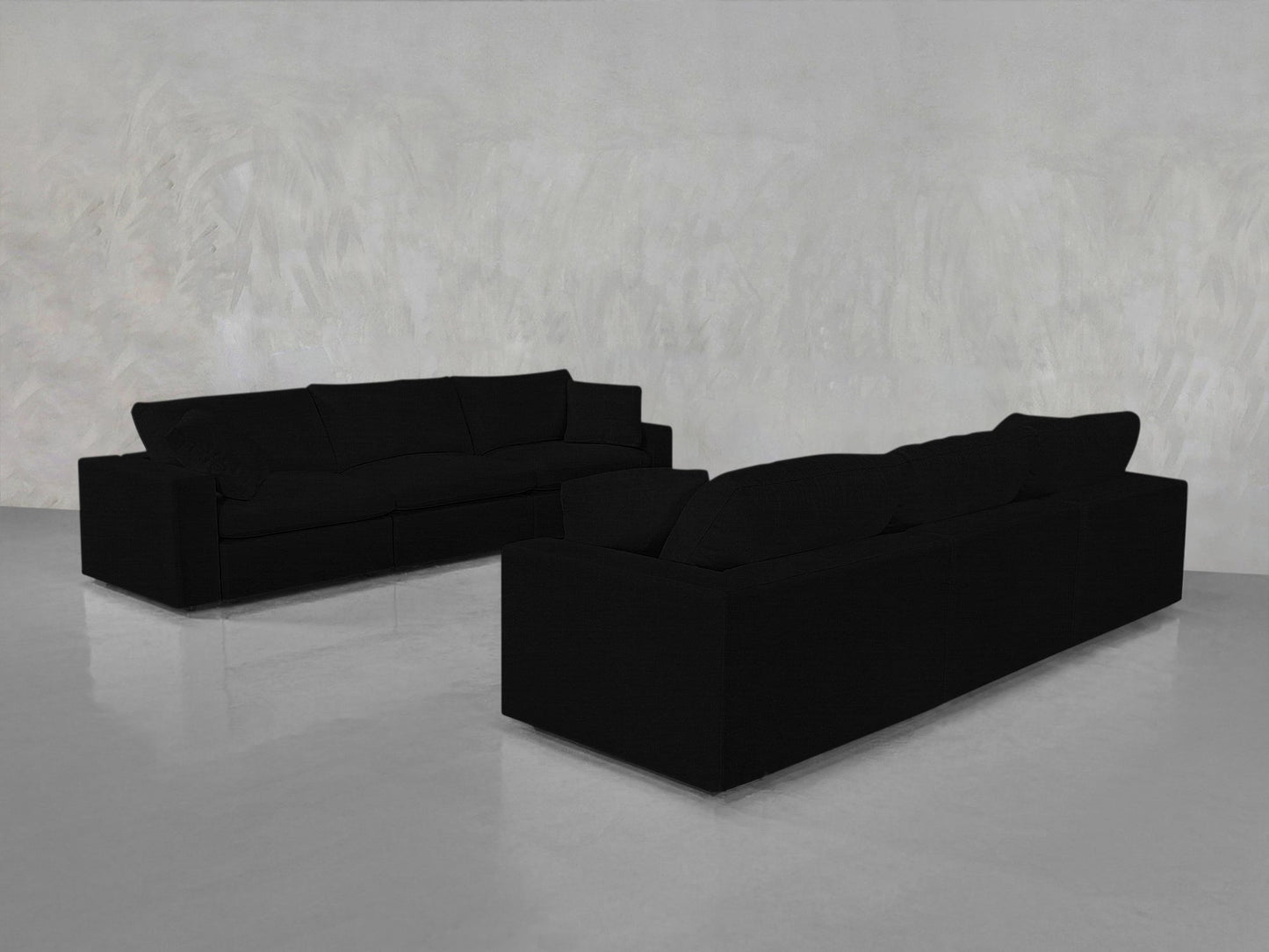 Two 3-3 Sofa Sets in large black are arranged facing each other at an angle in an empty room with light gray textured walls and a shiny, reflective floor.
