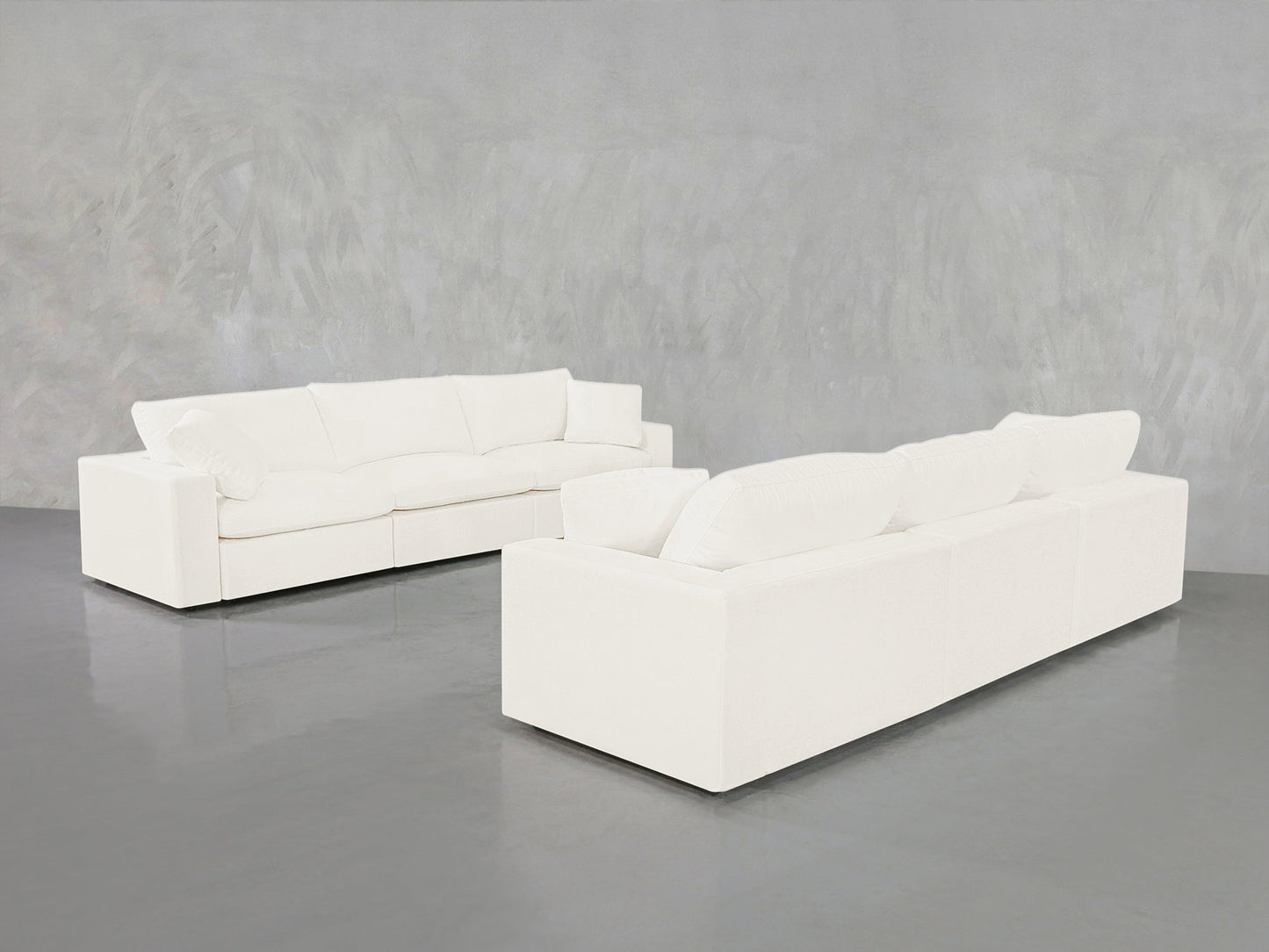 The 3-3 Sofa Set, featuring modern white sofas with clean lines and plush cushions, is arranged on a glossy gray floor against a light gray textured wall—one sofa facing forward, the other from behind.