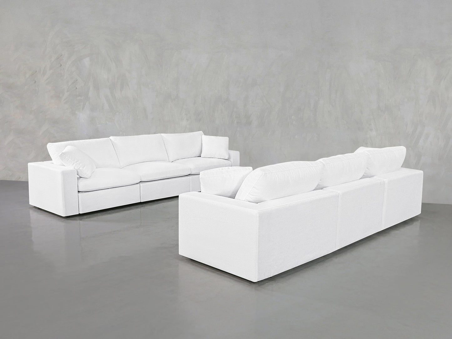 Two stylish 3-3 Sofa Sets with plush cushions stand on a shiny gray floor against a light gray textured wall, creating a minimalist atmosphere.