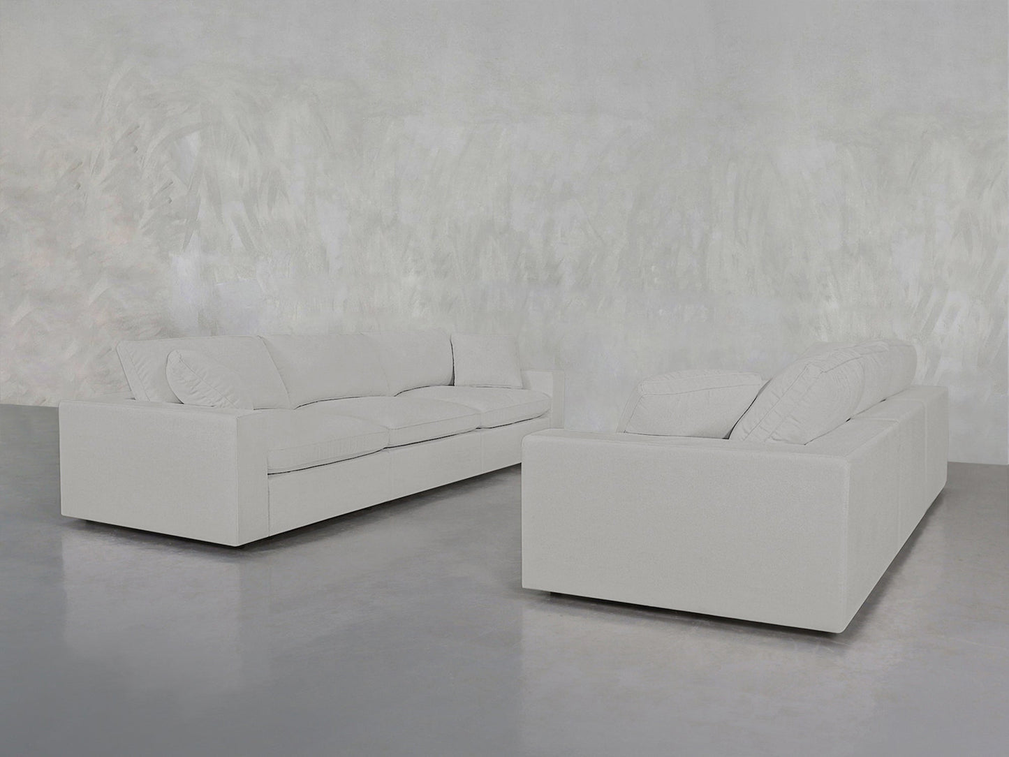 The 3-3 Sofa Set, featuring two modern light gray sofas with clean lines, is arranged facing each other on a polished concrete floor against a textured light gray wall.