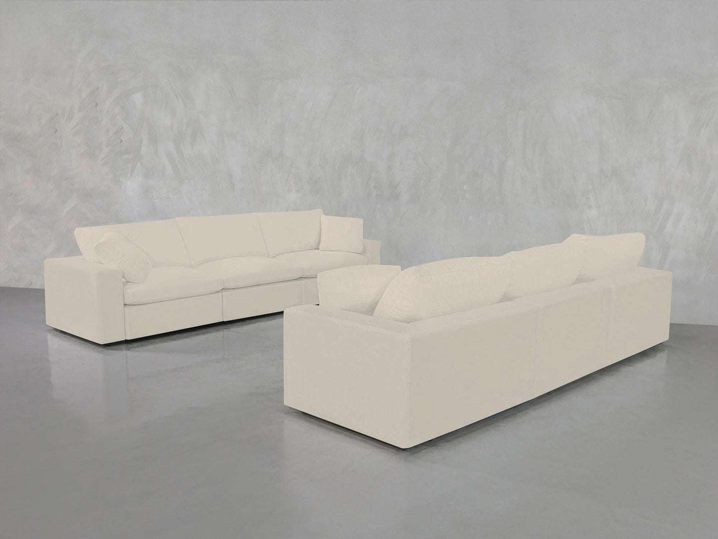 The 3-3 Sofa Set, featuring two modern white sofas with plush cushions, is arranged on a shiny gray floor against a textured light gray wall in a spacious, minimalist room.