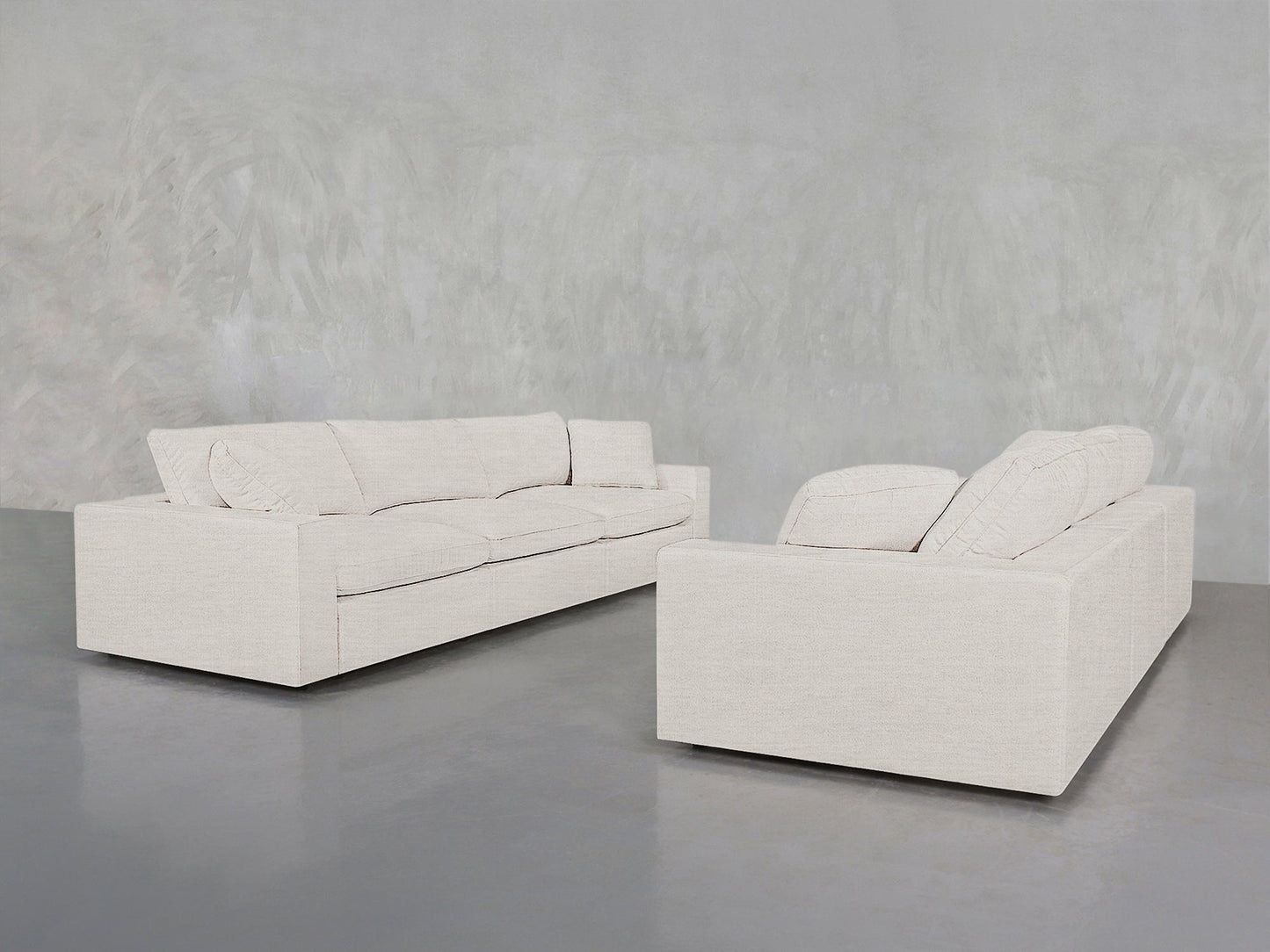 Two 3-3 Sofa Set pieces in light beige with clean lines and plush cushions are placed against a gray wall and polished concrete floor, creating a minimalist look.