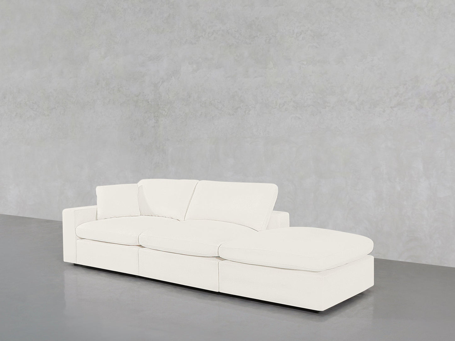 The 3-Seat Modular Lounger Sofa in modern white with a chaise lounge is placed on a polished gray floor against a light gray textured wall.