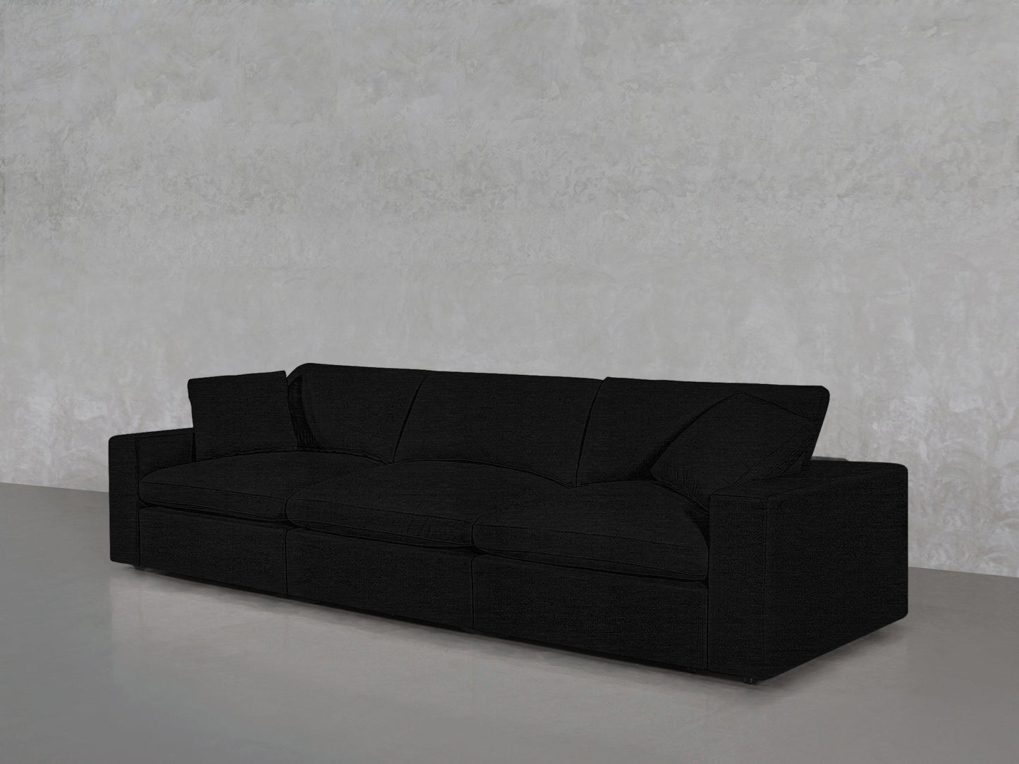 The 3-Seat Modular Sofa in modern black features clean lines and sits on a smooth gray floor against a textured light gray wall.