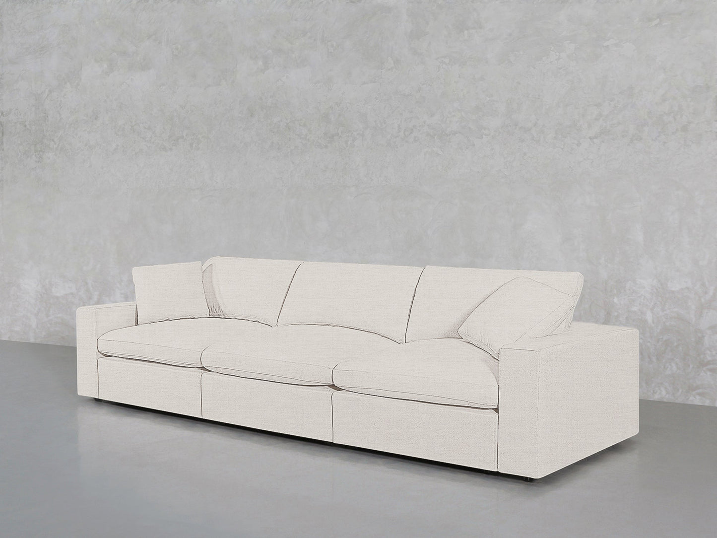 The 3-Seat Modular Sofa, featuring straight arms and plush cushions in white, is placed on a smooth gray floor against a textured light gray wall.