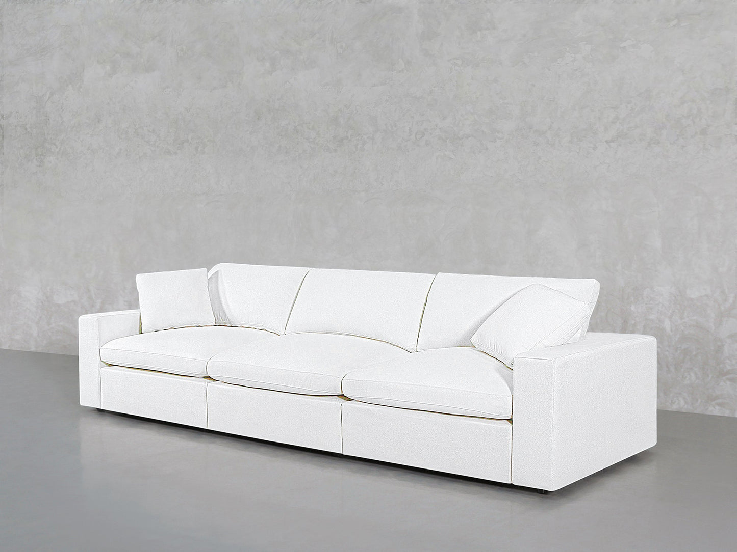 The 3-Seat Modular Sofa in modern white with boxy arms and two matching cushions is set against a plain, light gray textured wall on a smooth gray floor.