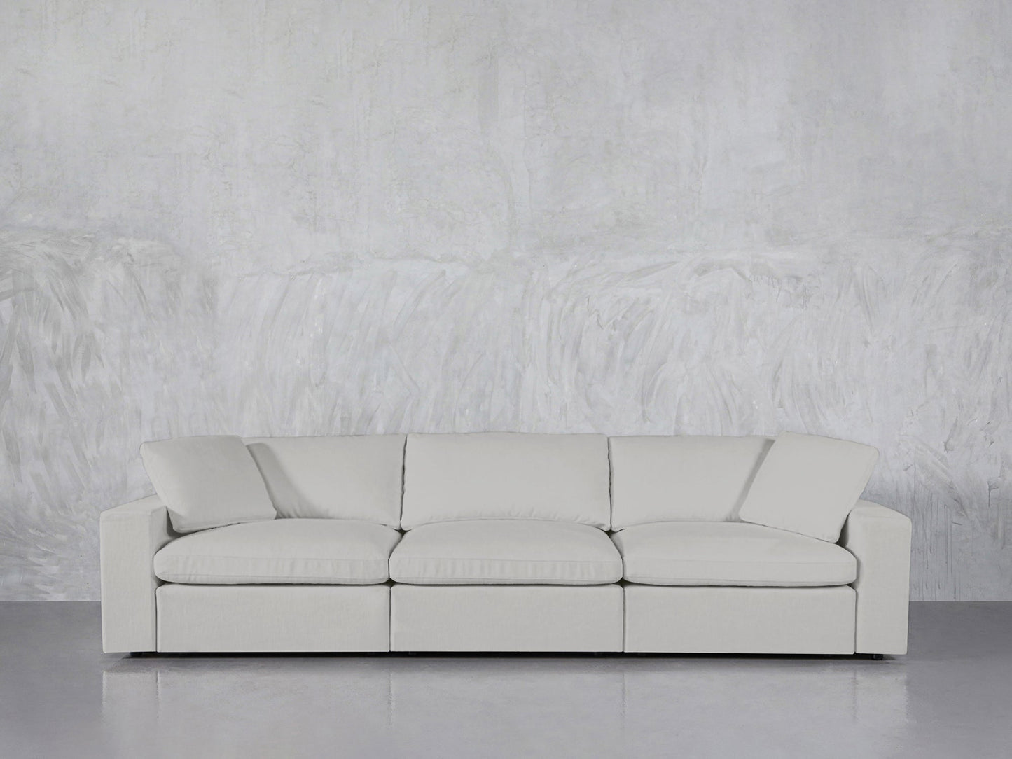 The 3-Seat Modular Sofa, featuring modern clean lines in light gray, sits against a textured gray wall atop a glossy floor.