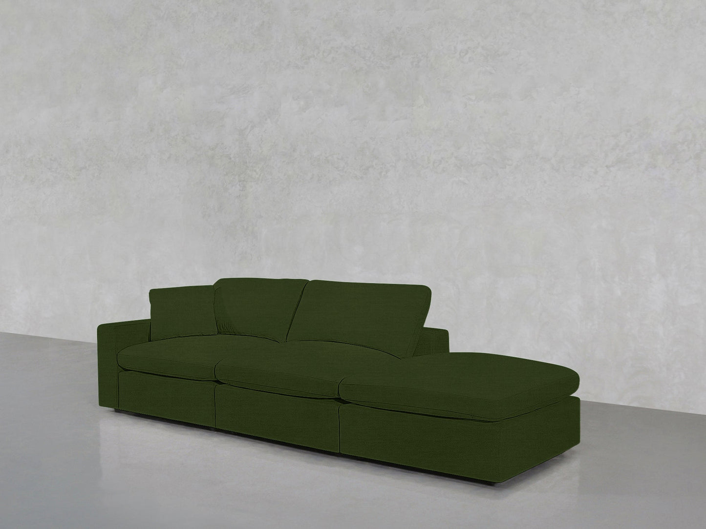 The 3-Seat Modular Lounger Sofa in green features three seats and a right-side chaise, placed before a plain light grey textured wall and a smooth grey floor.