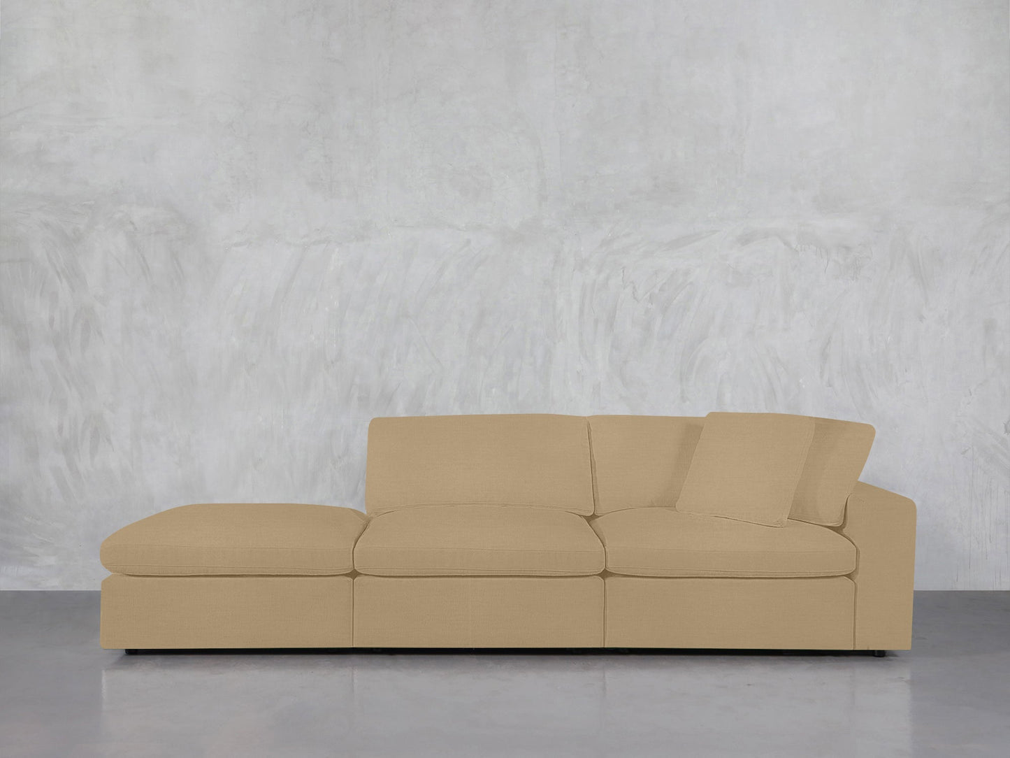A 3-Seat Modular Lounger Sofa in beige with simple cushions sits against a textured light gray wall on a smooth, reflective floor. One back cushion is slightly tilted.
