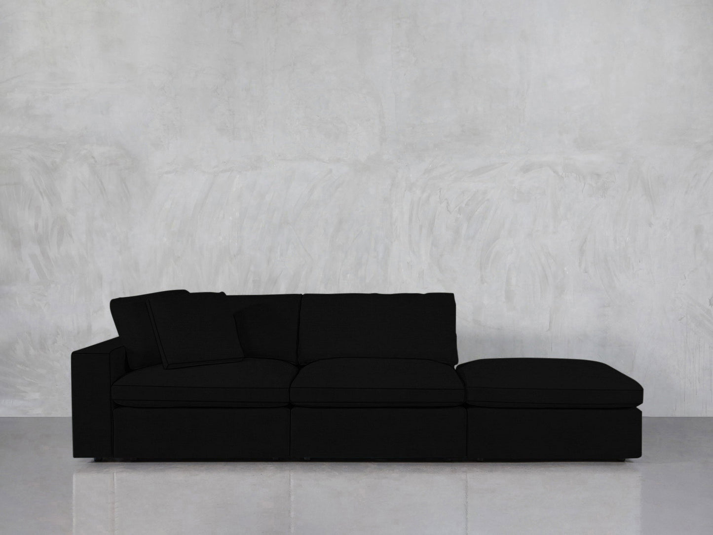 The 3-Seat Modular Lounger Sofa, featuring a sleek black finish and right-side chaise, is showcased against a light gray textured wall and a pale floor.