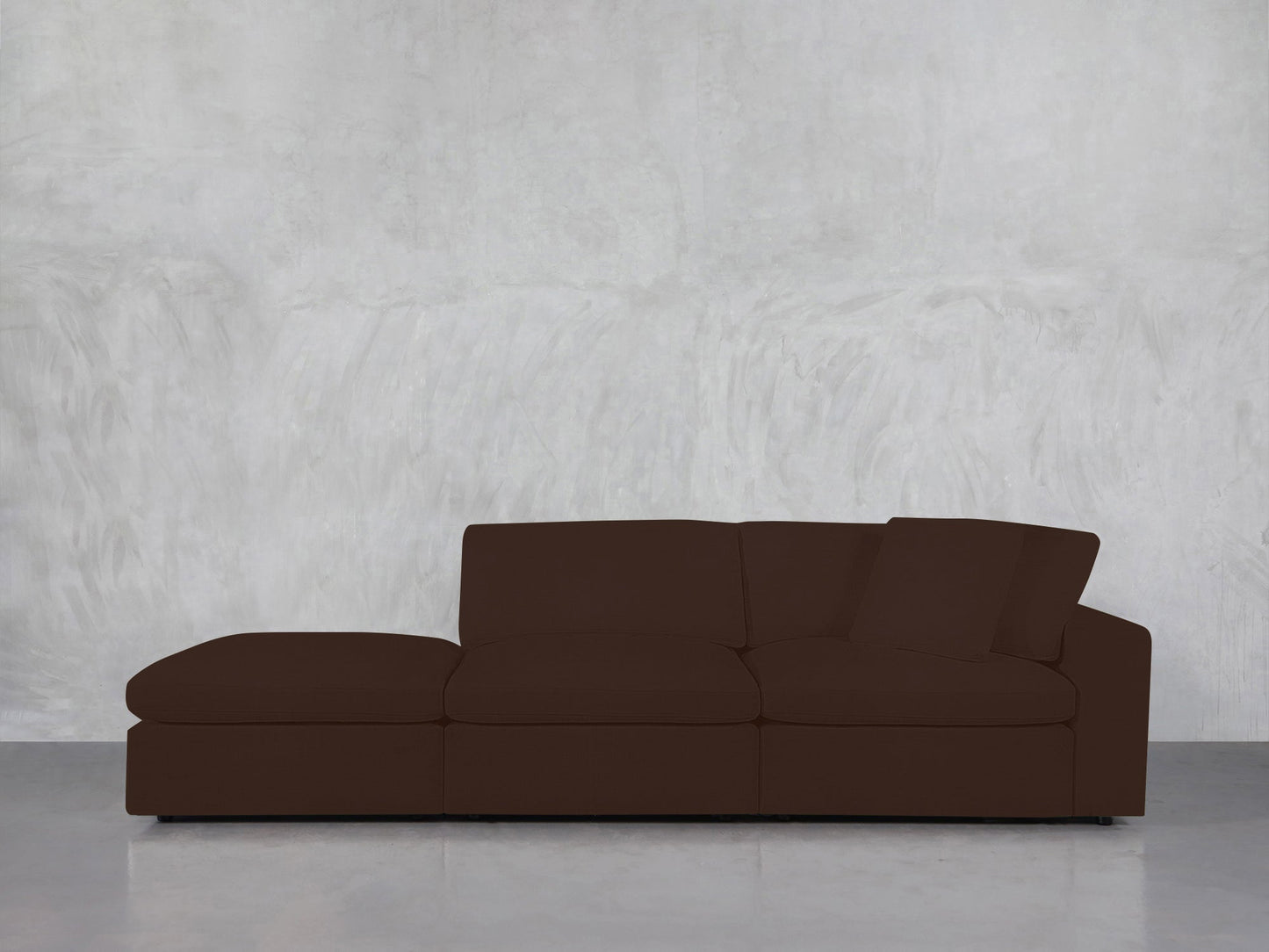 A 3-Seat Modular Lounger Sofa in brown is positioned against a light gray textured wall on a smooth, reflective floor.