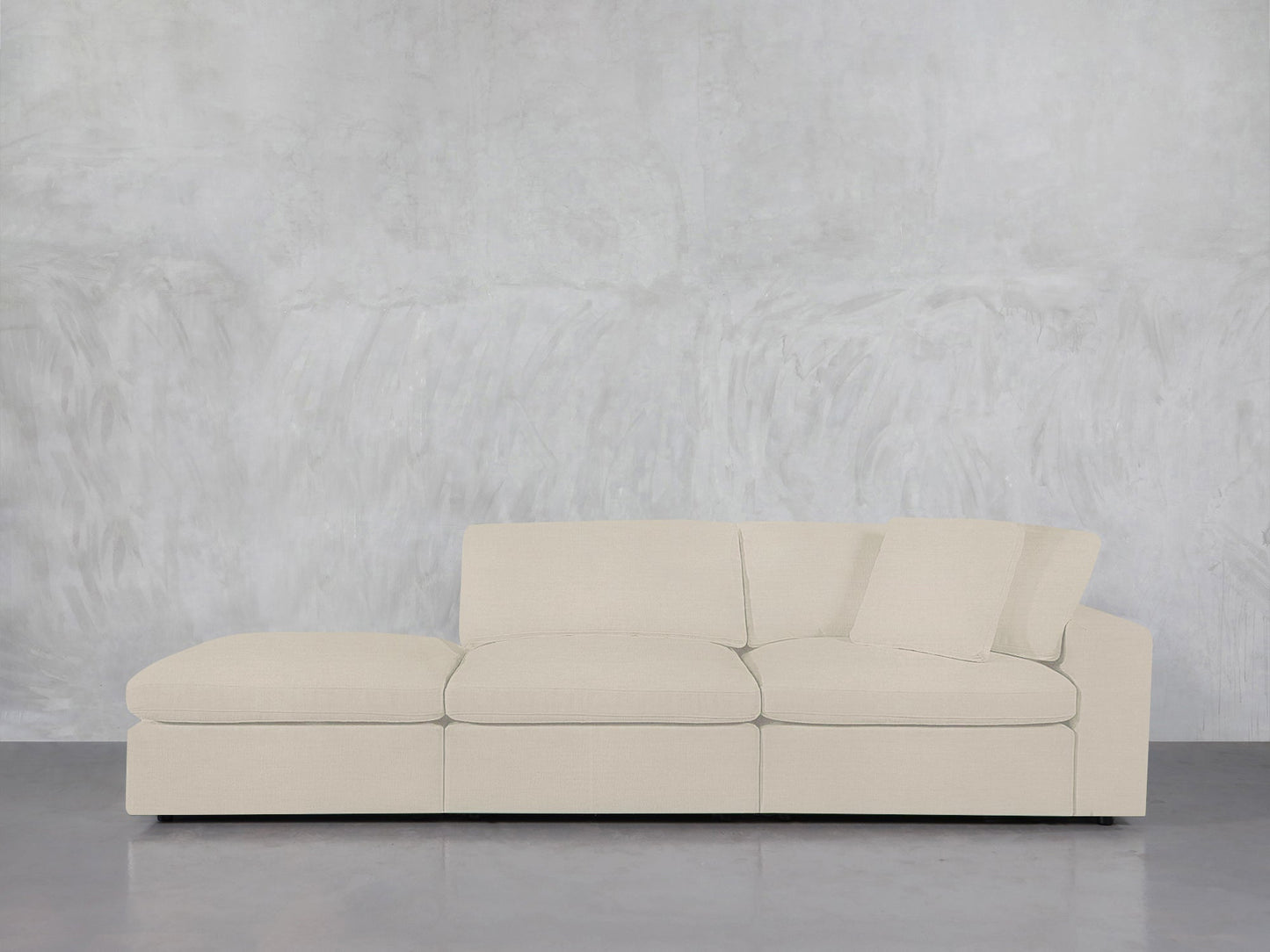 The 3-Seat Modular Lounger Sofa in light beige, featuring three seat and back cushions, is placed against a minimalist gray textured wall and a polished gray floor.