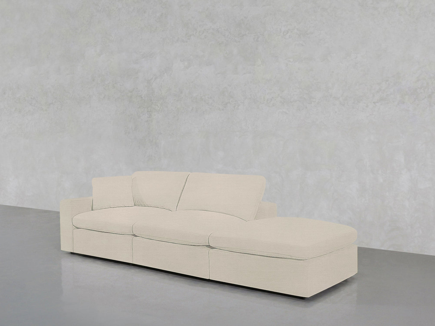 The 3-Seat Modular Lounger Sofa in light beige features three seat cushions and a right chaise, set against a textured pale gray wall on a polished gray floor.