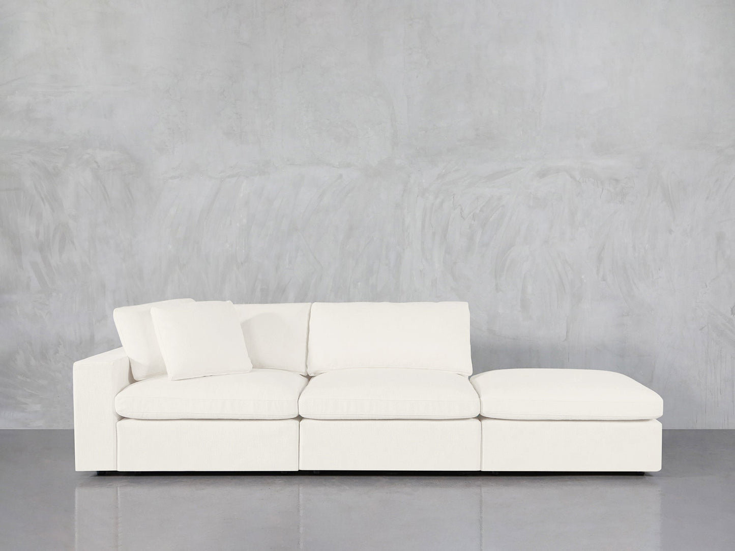 The 3-Seat Modular Lounger Sofa, featuring a modern white design with three seat cushions and one back cushion, sits against a light gray textured wall on a polished concrete floor.