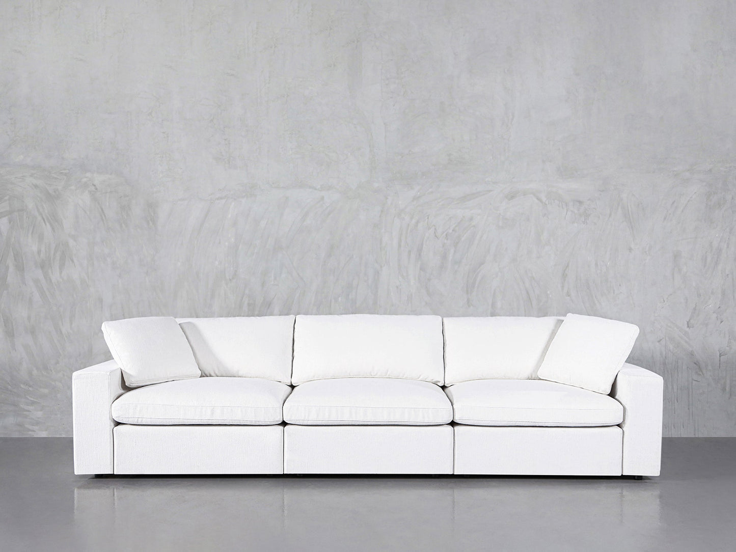 A 3-Seat Modular Sofa in modern white, featuring straight arms and three seat cushions, sits against a light gray textured wall on a shiny gray floor.