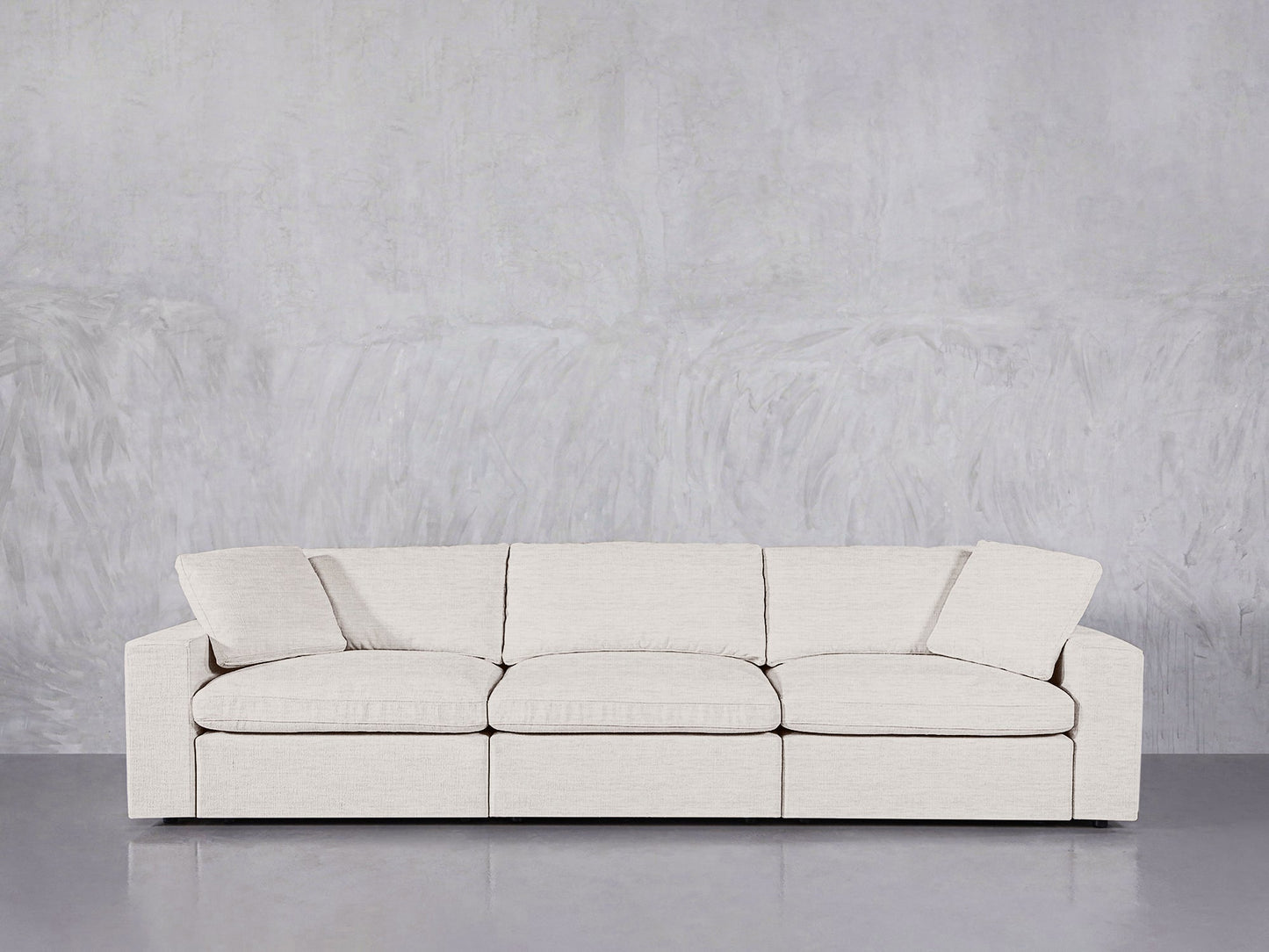 The 3-Seat Modular Sofa in modern beige, featuring three seat cushions and two armrests, sits against a textured light gray wall on a sleek, glossy gray floor.