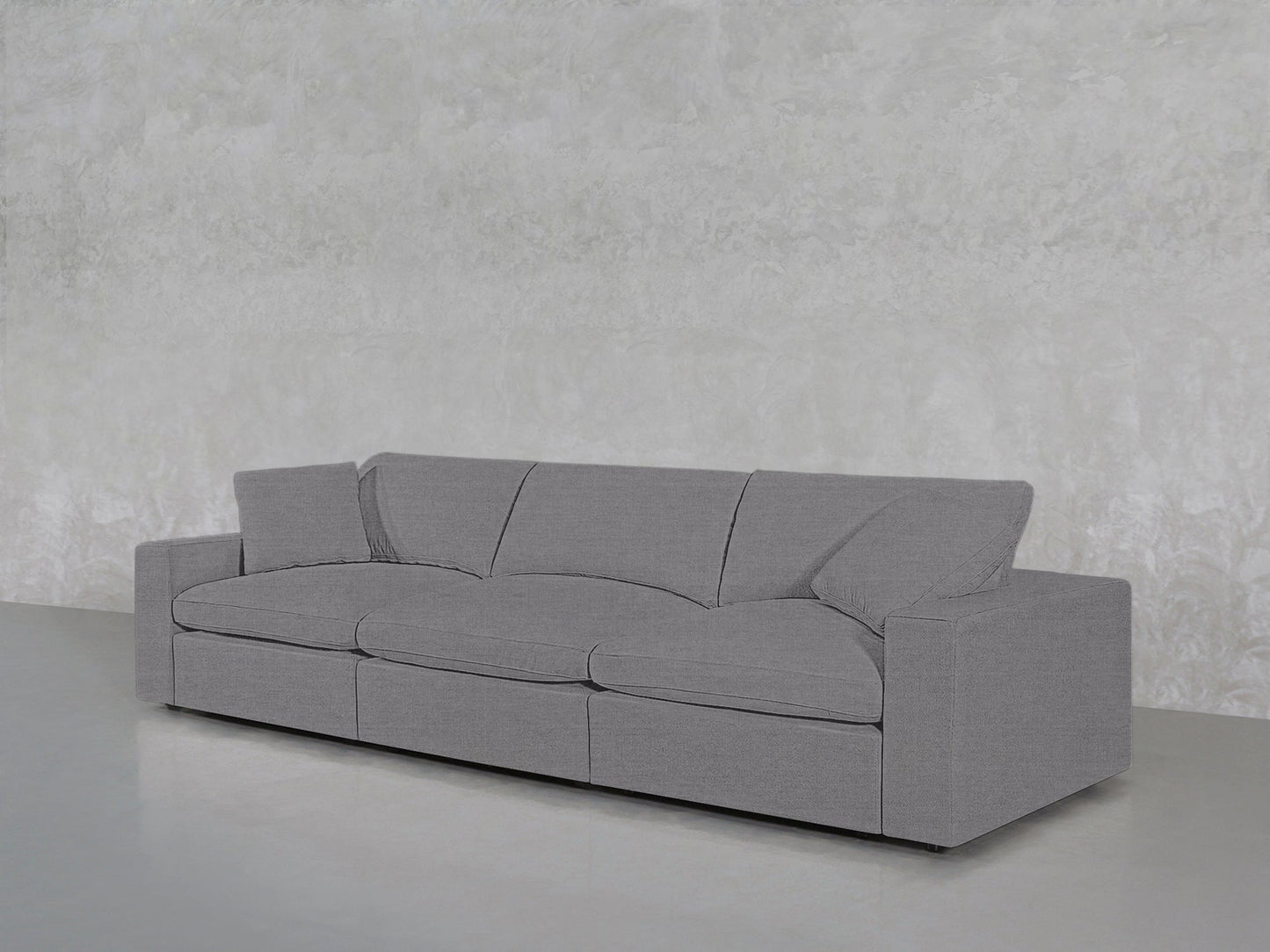 A 3-Seat Modular Sofa in modern grey with square arms and plush cushions is set against a textured light grey wall on a smooth, light floor.