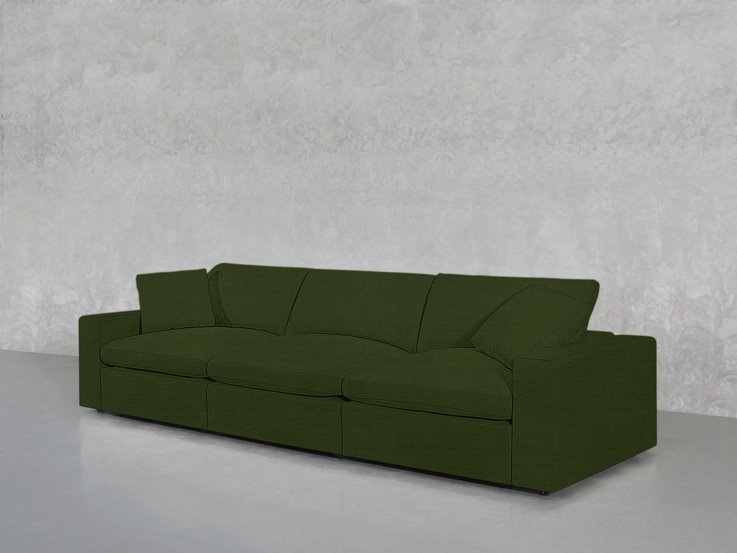 The 3-Seat Modular Sofa in dark green, featuring wide armrests, stands against a light gray textured wall on a smooth, light gray floor.