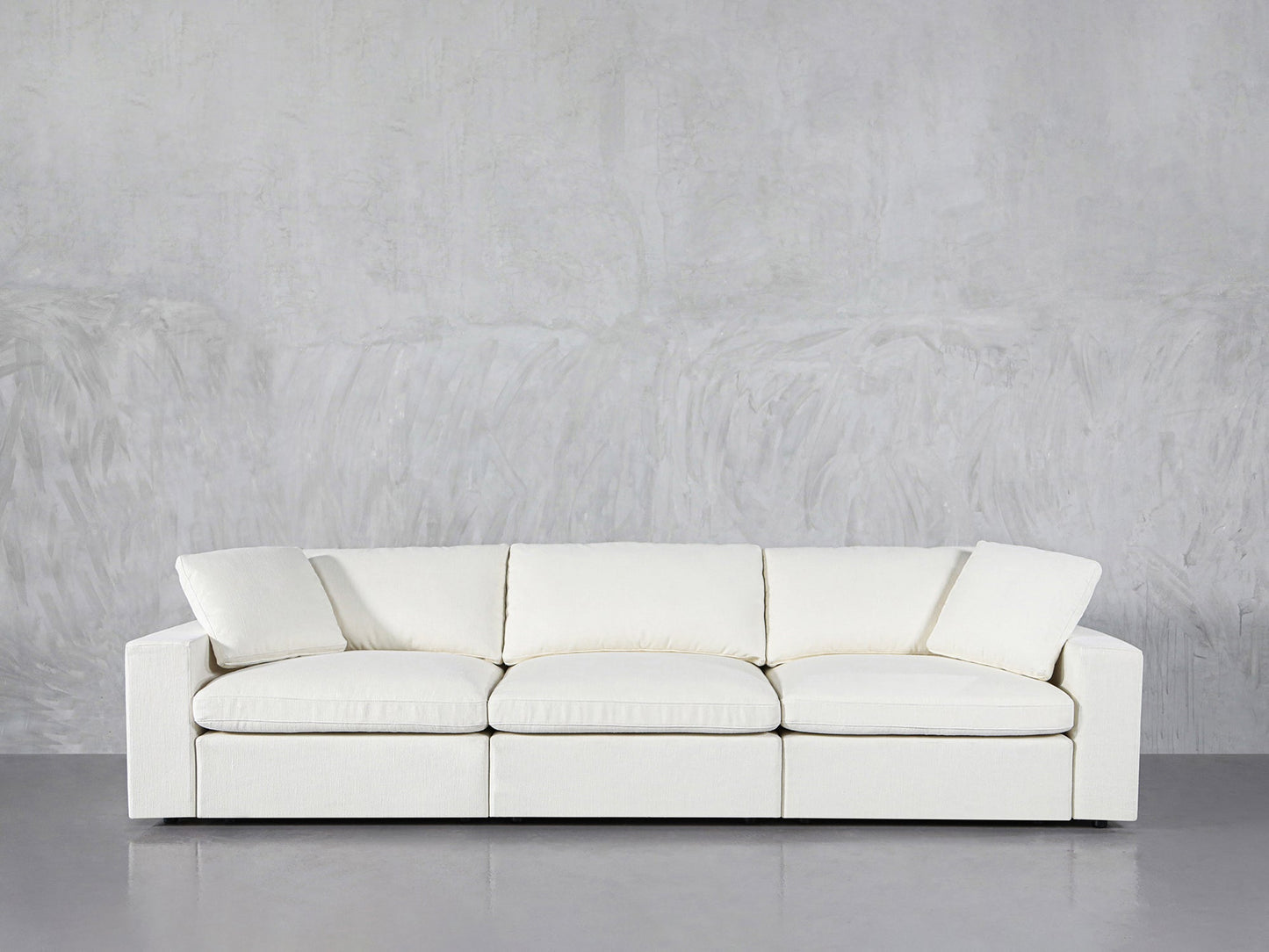 The 3-Seat Modular Sofa with clean lines and plush cushions, in modern white, is set against a light gray textured wall on a smooth gray floor.