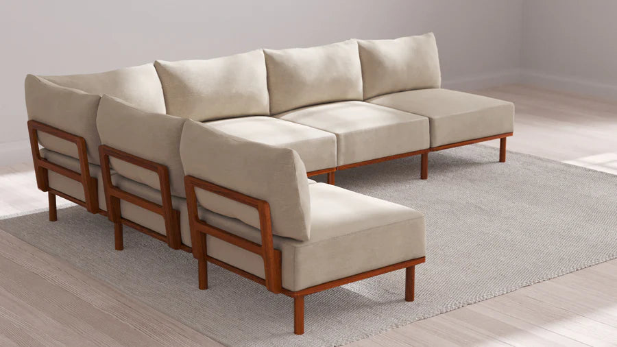 An Indoor Jack 6-Seater Open-Ends Corner Sectional in Balsa is arranged on a light gray area rug in a bright room with white walls and a hardwood floor.