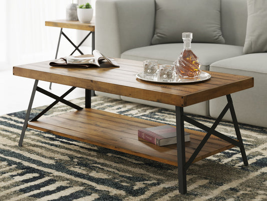 The Douglas Coffee Table features a wooden top and metal frame, holding a tray with a decanter and glasses, an open magazine, and books on the lower shelf. A sofa and side table sit behind it, all atop a patterned rug.