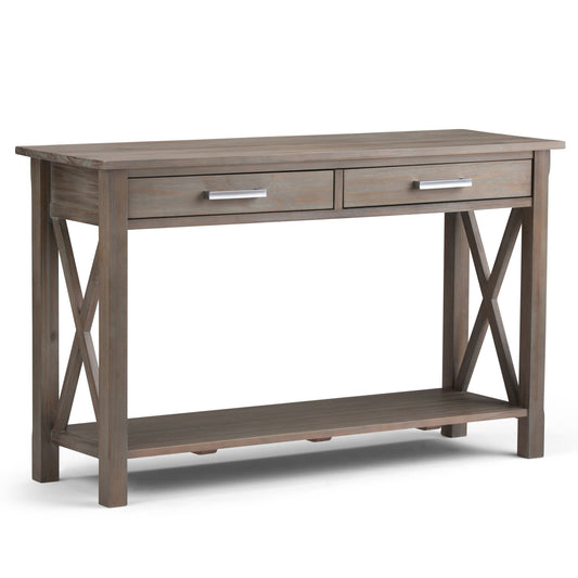 The Kitchener - Handcrafted Table features a weathered wood finish, two front drawers with silver handles, X-shaped side supports, and an open lower shelf.