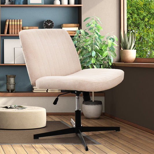 The Cross Legged Office Chair in beige with a black metal base is placed on a dark mat in a cozy room with wooden floors, bookshelves, potted plants, and a window revealing greenery outside.