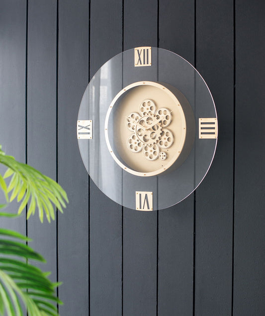 The Round Moving Gear Roman Numeral Clock - Multicolor features visible cream gears and Roman numerals, mounted on a dark, vertically paneled wall with green plant leaves in the lower left corner.
