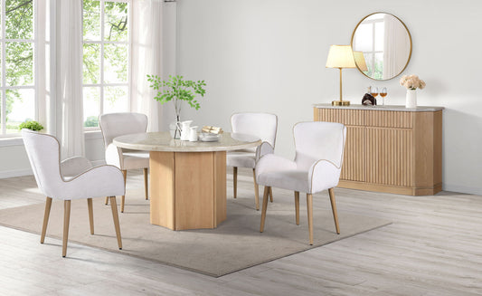 A modern dining room featuring the Qwin Marble Top Round Dining Table in Natural, surrounded by four white upholstered chairs, a beige rug, a sideboard with a lamp and flowers, a round mirror, and large windows for natural light.