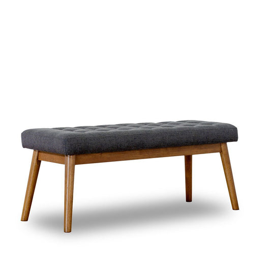 The Delilah - Modern Bench - Gray features a cushioned, dark gray tufted seat and angled wooden legs, showcased against a white background in a sleek mid-century modern style.