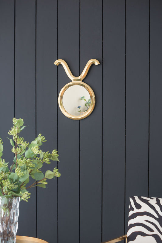 A Modern Round Mirror With Aluminum Frame, Wall Decor For Entryway Living Room Hallway - Gold hangs on a dark wood panel wall. In front, there’s a plant in a glass vase and a chair with a zebra-patterned cushion.