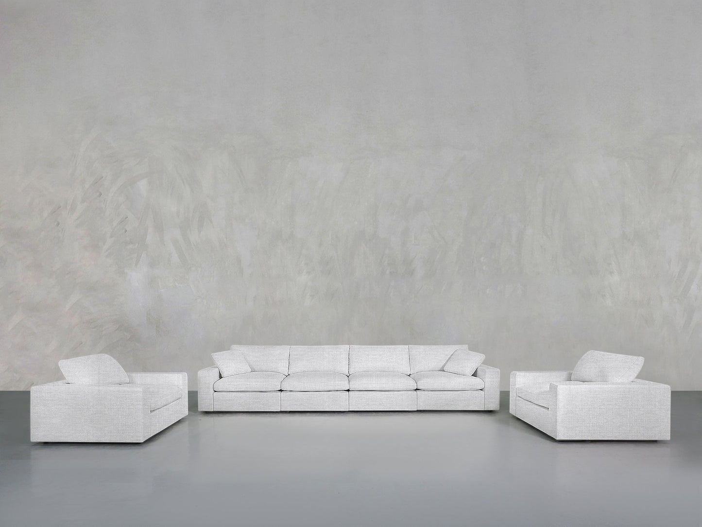 The 4-1-1 Sofa & Armchair Set features a light gray three-seater sofa and two matching armchairs, arranged on a smooth gray floor against a large textured gray wall for a minimalist living room look.
