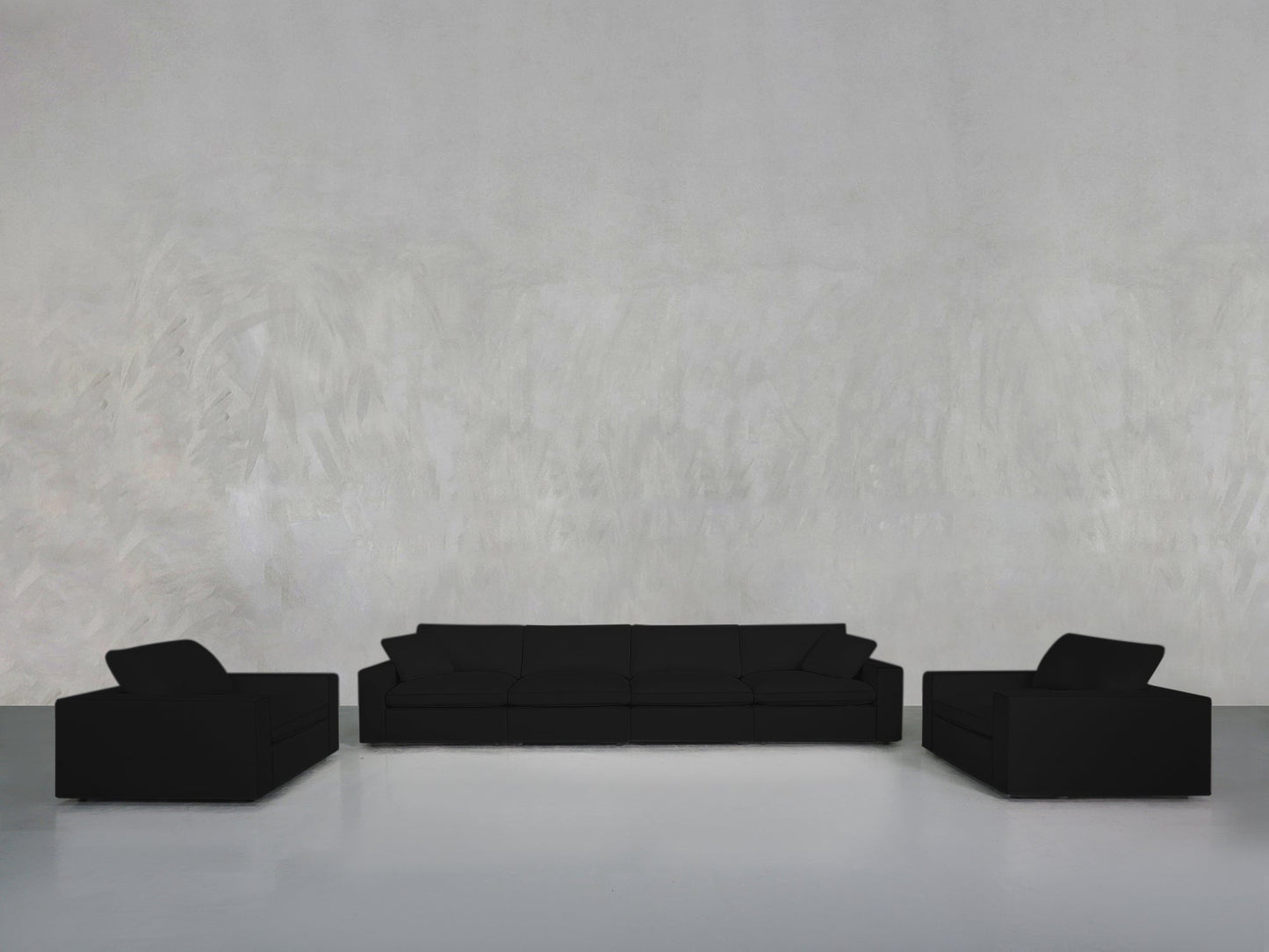A minimalist room with a light gray textured wall, centered around the 4-1-1 Sofa & Armchair Set in black—three-seat sofa and two matching armchairs facing each other. The floor is smooth and reflective.