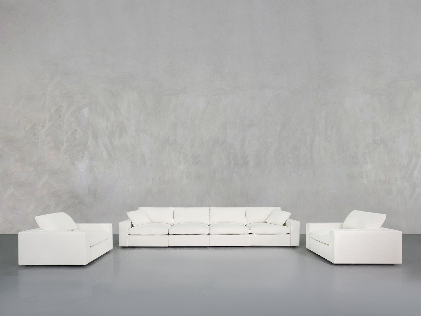 Minimalist room featuring the 4-1-1 Sofa & Armchair Set—a large, modern white sofa centered between two matching white armchairs—set against a plain, light gray textured wall and gray floor.