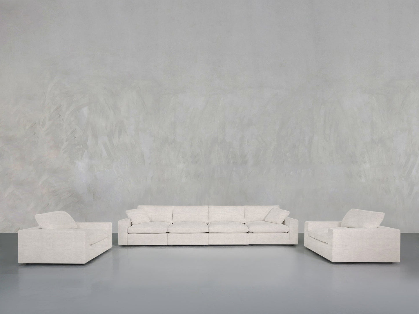 The 4-1-1 Sofa & Armchair Set, featuring a central three-seater and two single armchairs in light grey upholstery, is arranged against a minimalist grey textured wall and floor backdrop.