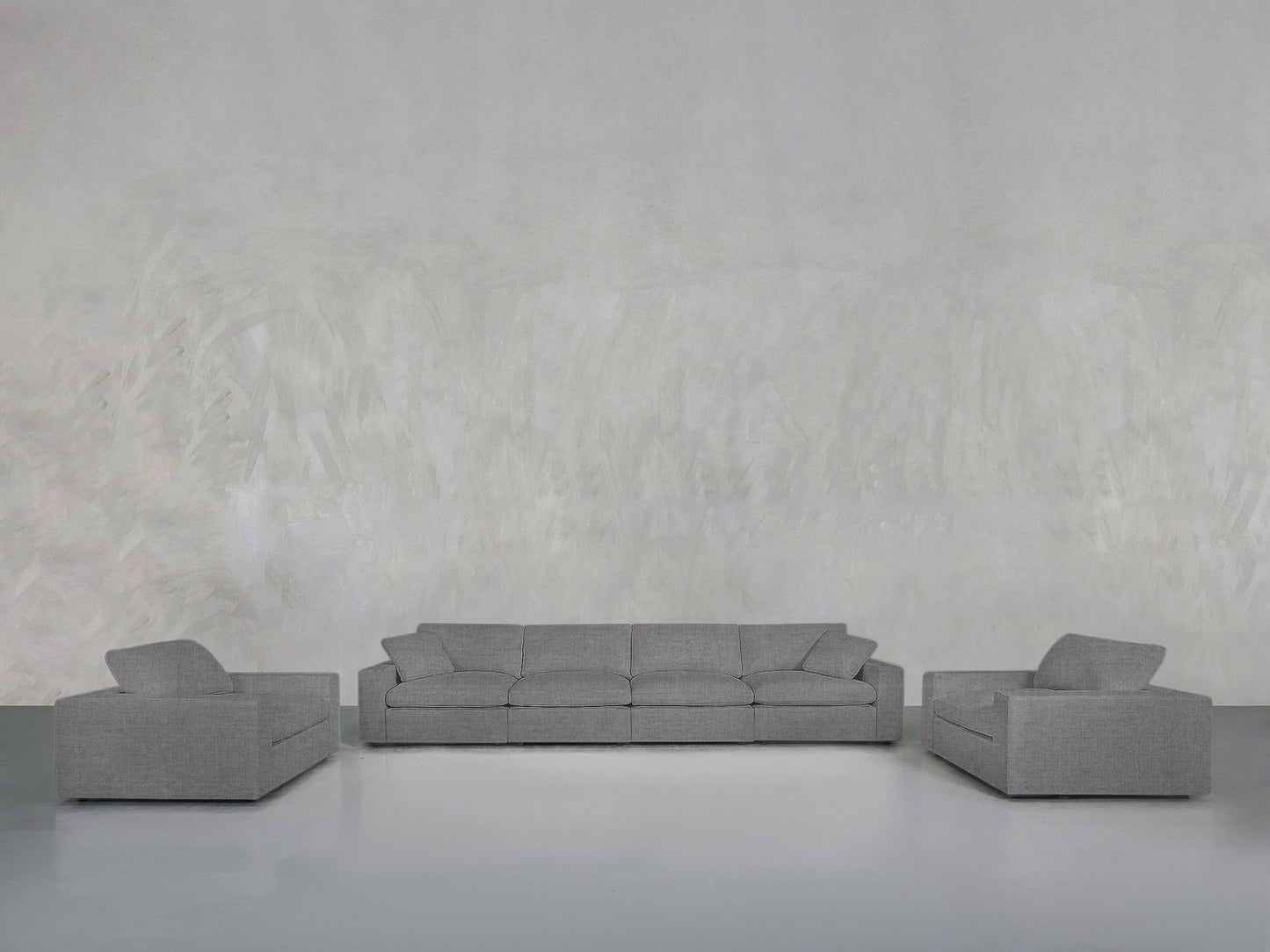 A minimalist room with a light gray textured wall, showcasing the 4-1-1 Sofa & Armchair Set: a matching gray three-seater sofa centered and two gray armchairs symmetrically placed on either side.