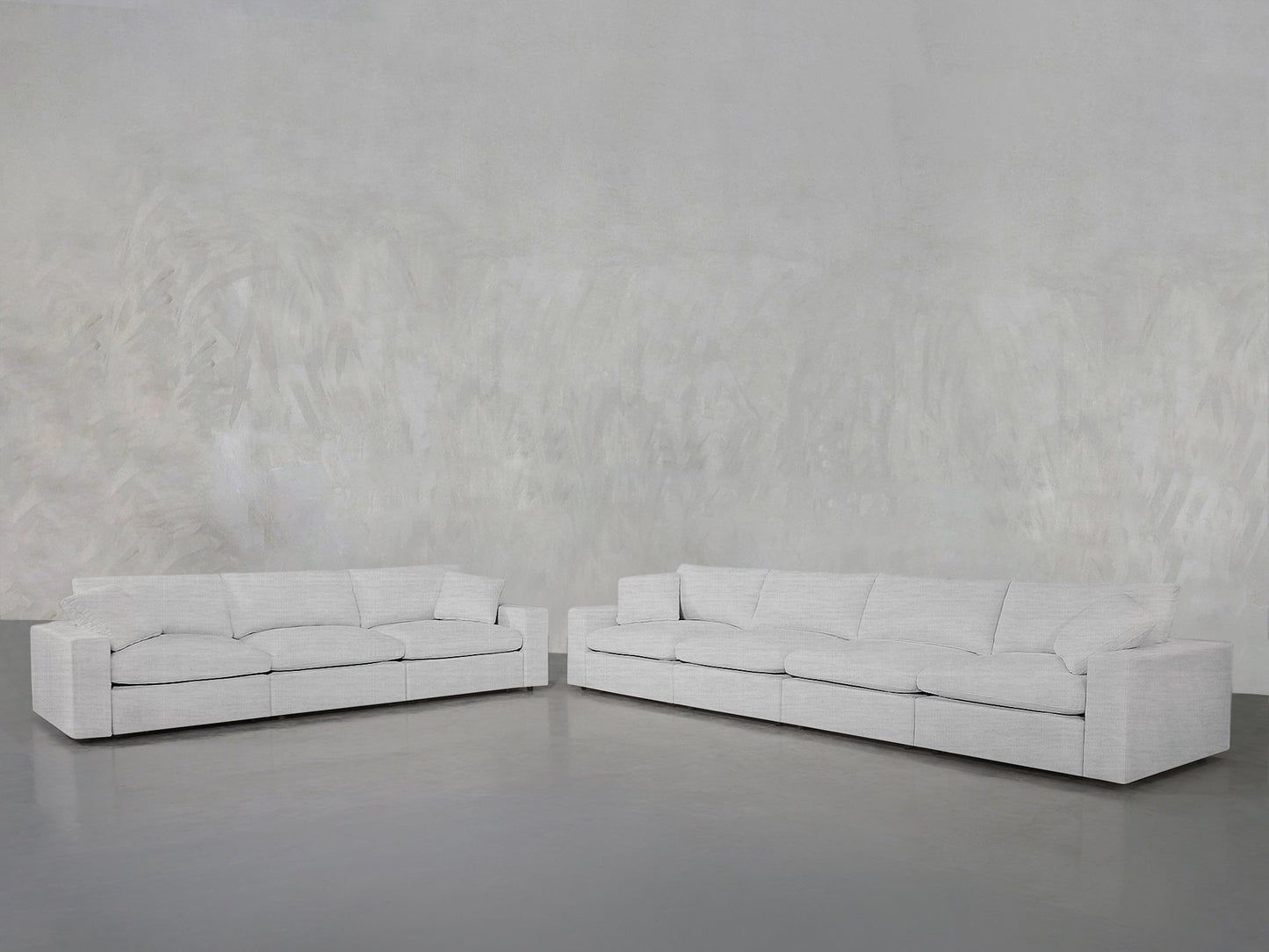 Two large, light gray 4-3 Sofa Set pieces are arranged in an L-shape against a textured, light gray wall and floor, creating a minimalist and spacious interior setting.