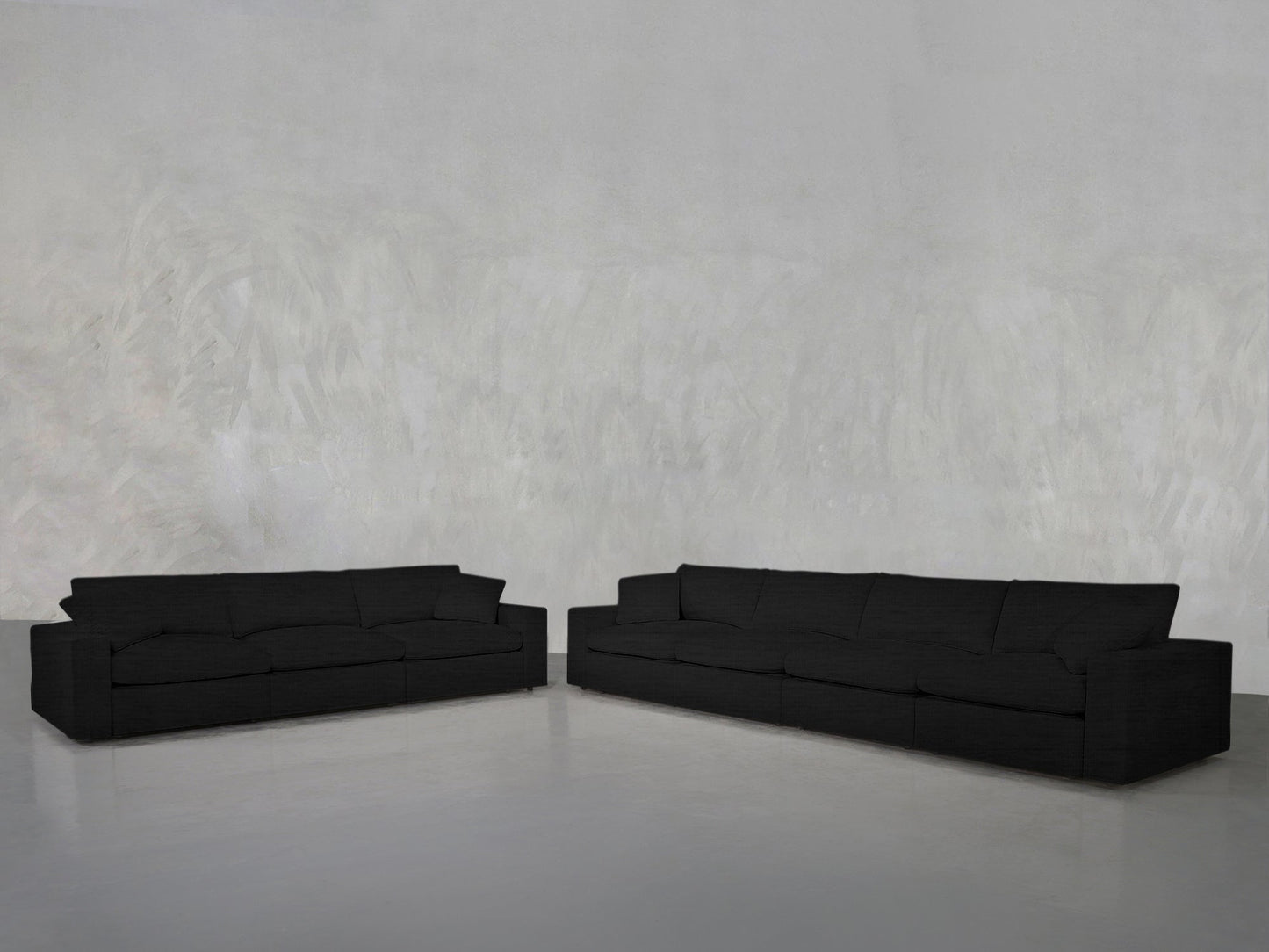 The 4-3 Sofa Set, featuring a modern black design, is arranged at an angle in an empty room with a light gray textured wall and smooth gray floor to create an inviting corner seating area.