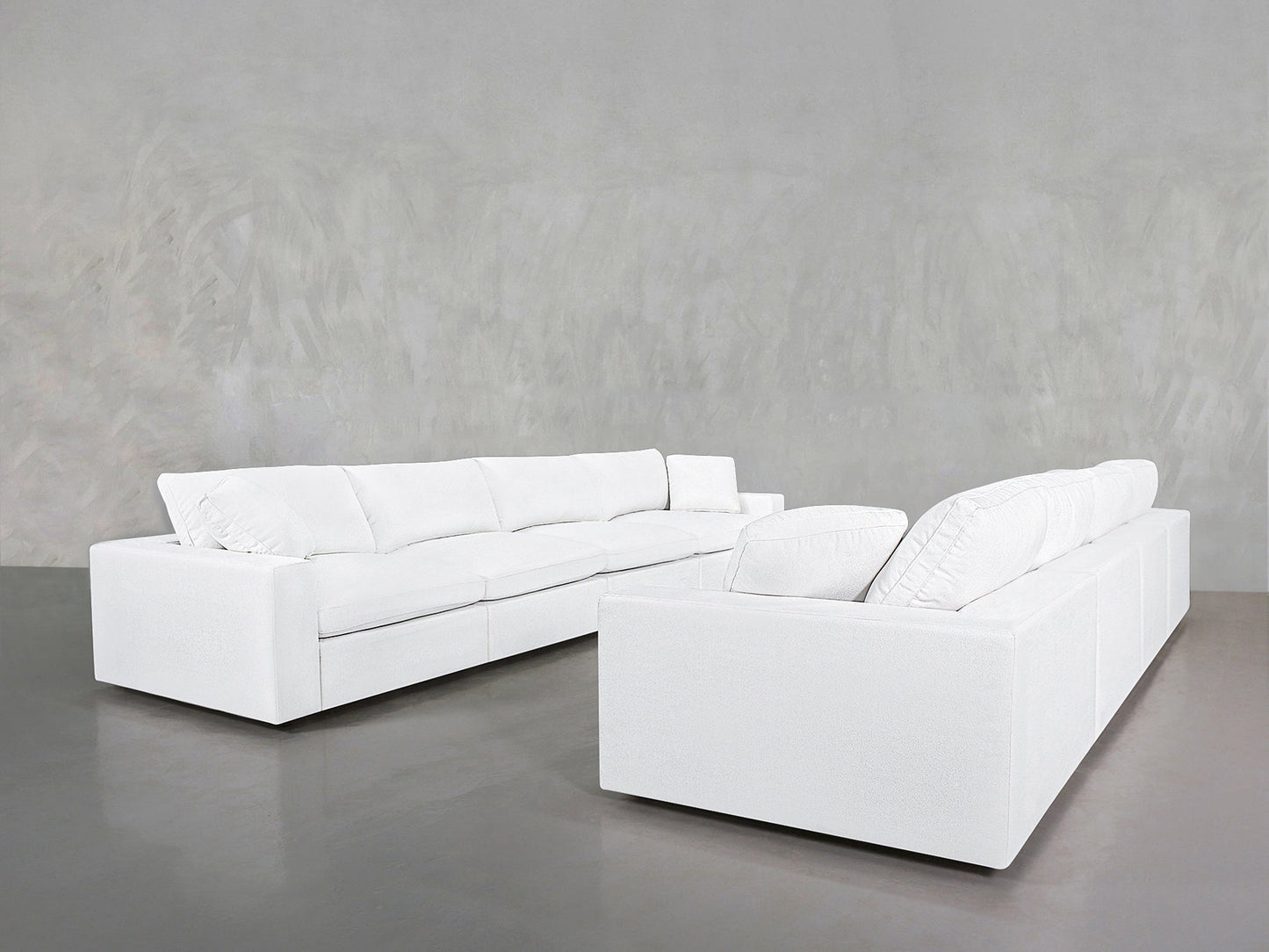 Two 4-4 Sofa Sets with modern white upholstery and plush cushions are arranged on a smooth grey floor, set against a light grey textured wall.