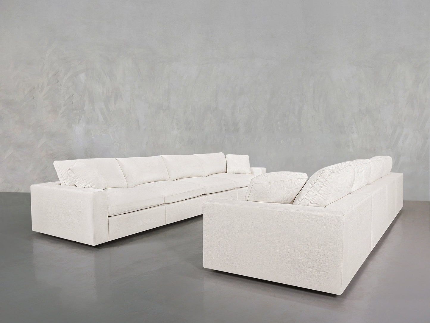 Two 4-4 Sofa Sets with clean lines and plush cushions are arranged on a gray polished floor against a light gray textured wall.