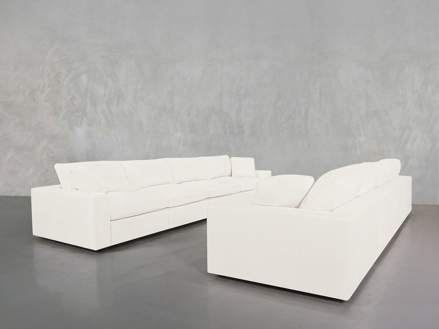 The 4-4 Sofa Set features two large white sectionals arranged in an L-shape on a polished gray floor, set against a light gray textured wall. Its clean, modern lines and plush cushions offer both style and comfort.