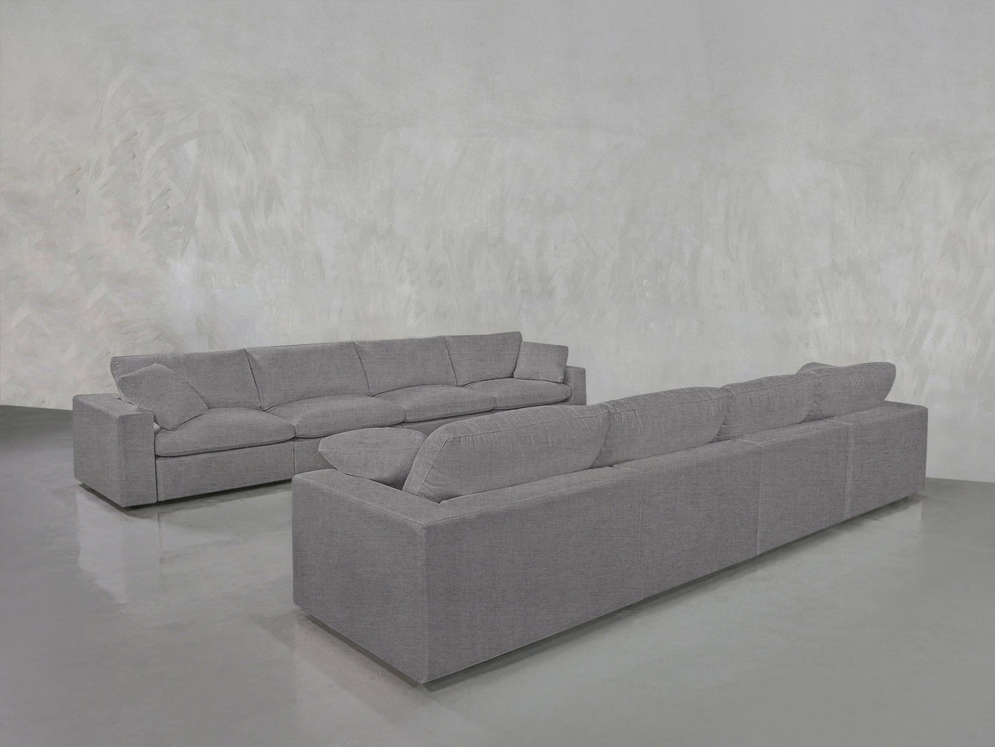 Two large, modern gray 4-4 Sofa Set sectionals with plush cushions are arranged in an L-shape on a shiny light gray floor against a textured light gray wall.