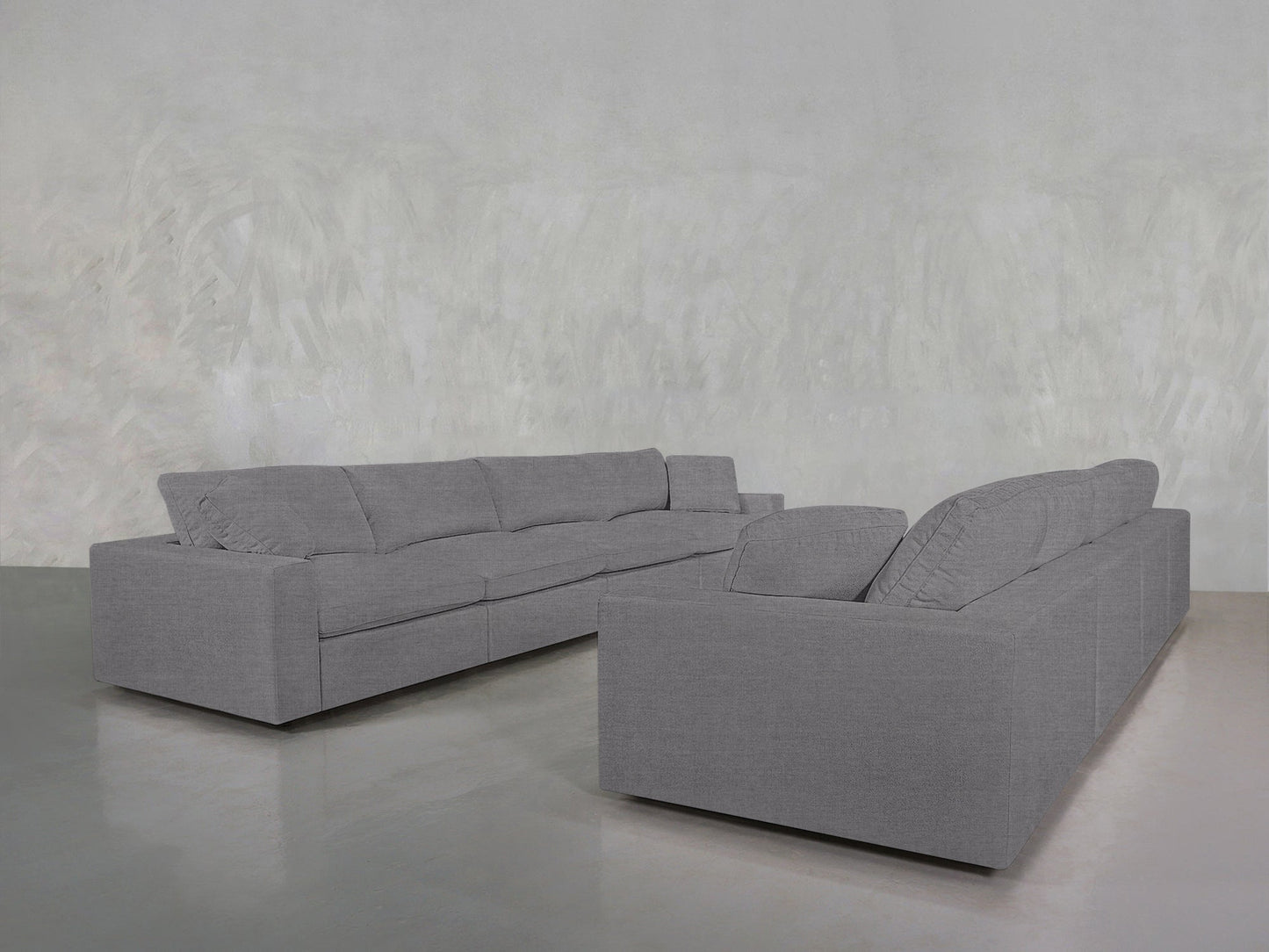 Two 4-4 Sofa Sets in gray are arranged in an L-shape in a minimalist room with light gray walls and a shiny, reflective floor.