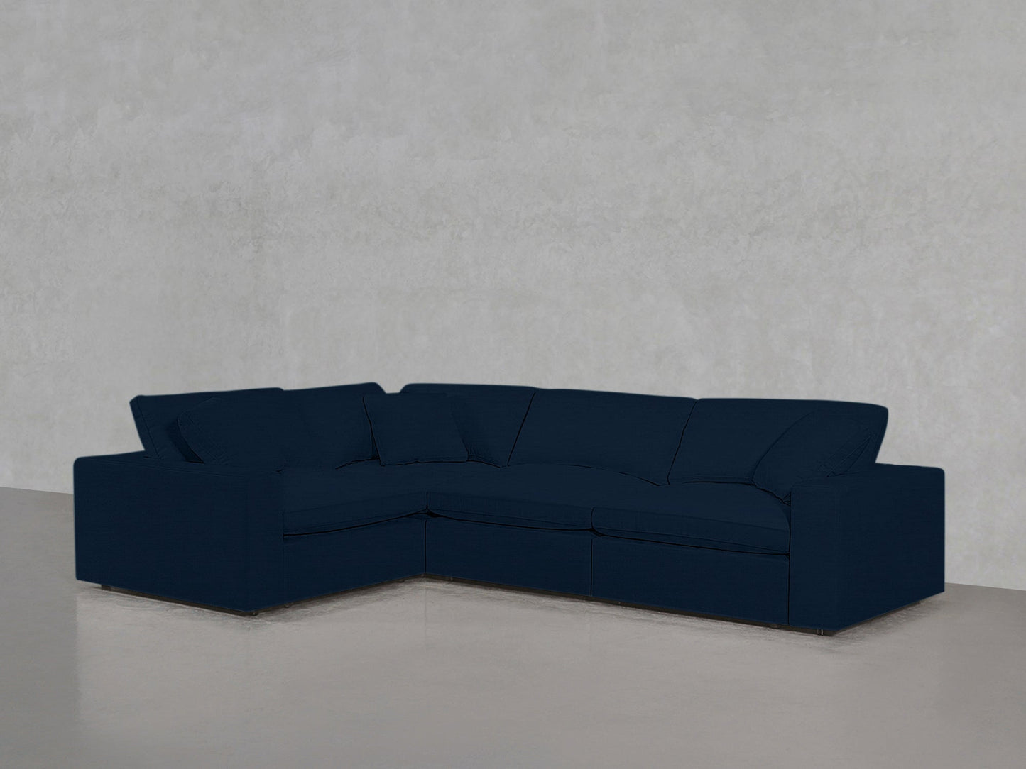 A 4-Seat Modular Corner Sectional in dark blue is positioned against a light gray textured wall on a smooth, light-colored floor.