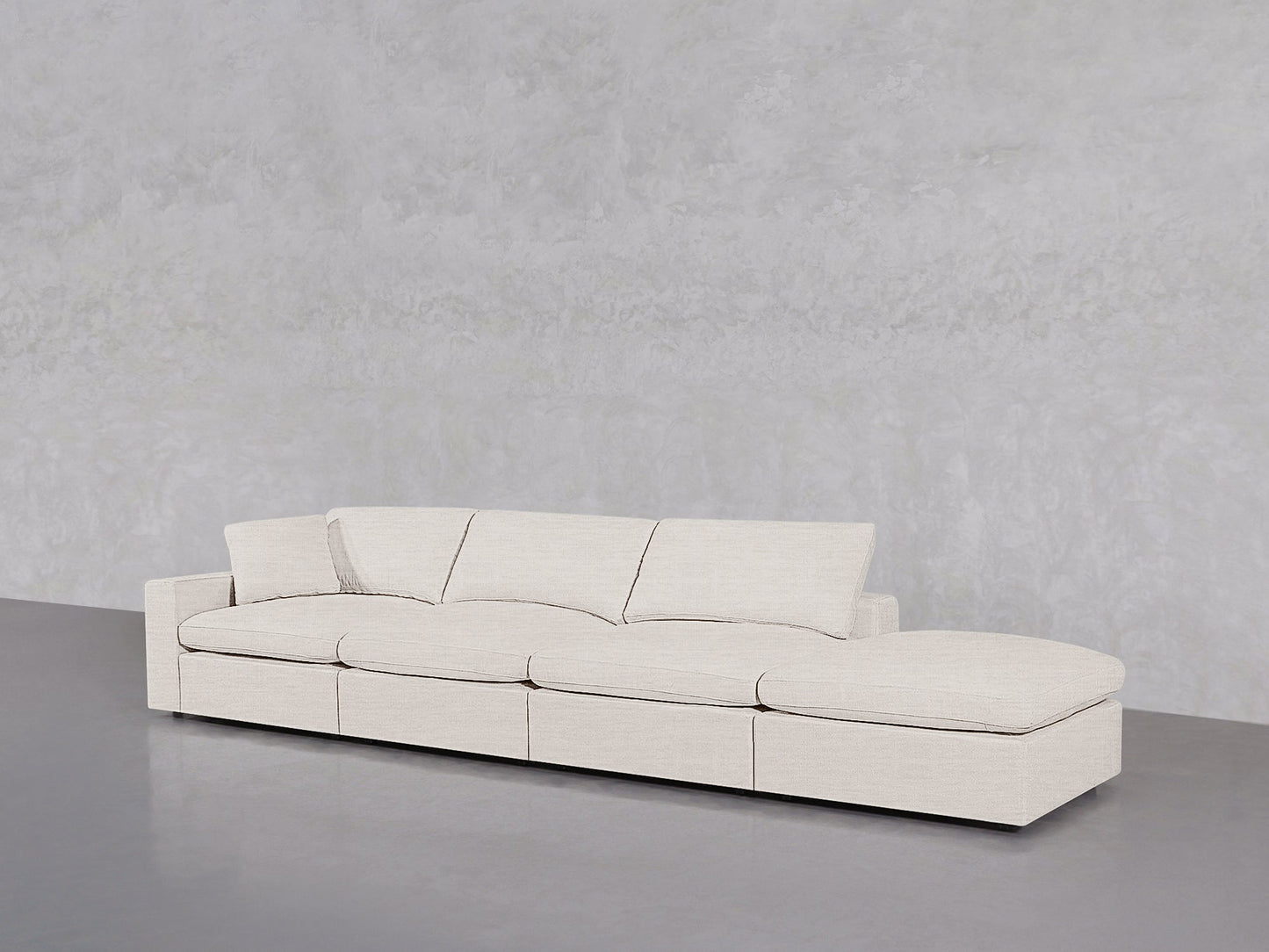 The 4-Seat Modular Lounger Sofa, in modern minimalist light beige, features four seat cushions and a right-side chaise lounge, placed against a plain light gray textured wall and smooth gray floor.